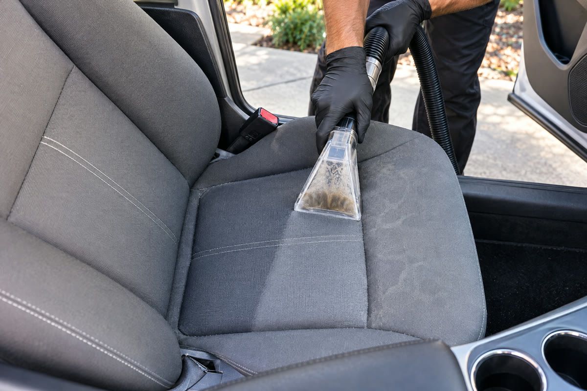 An extractor wand pulling dirty water out of a gray cloth seat