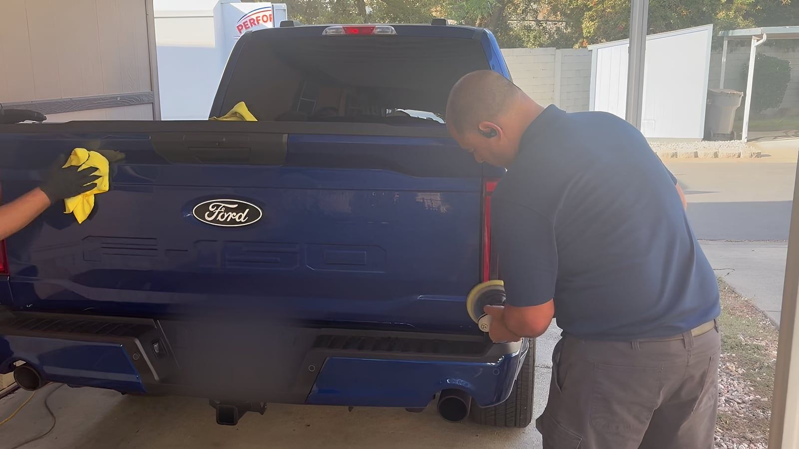 Lalo machine-polishing the tailgate corner of a blue Ford F-150 under a carport