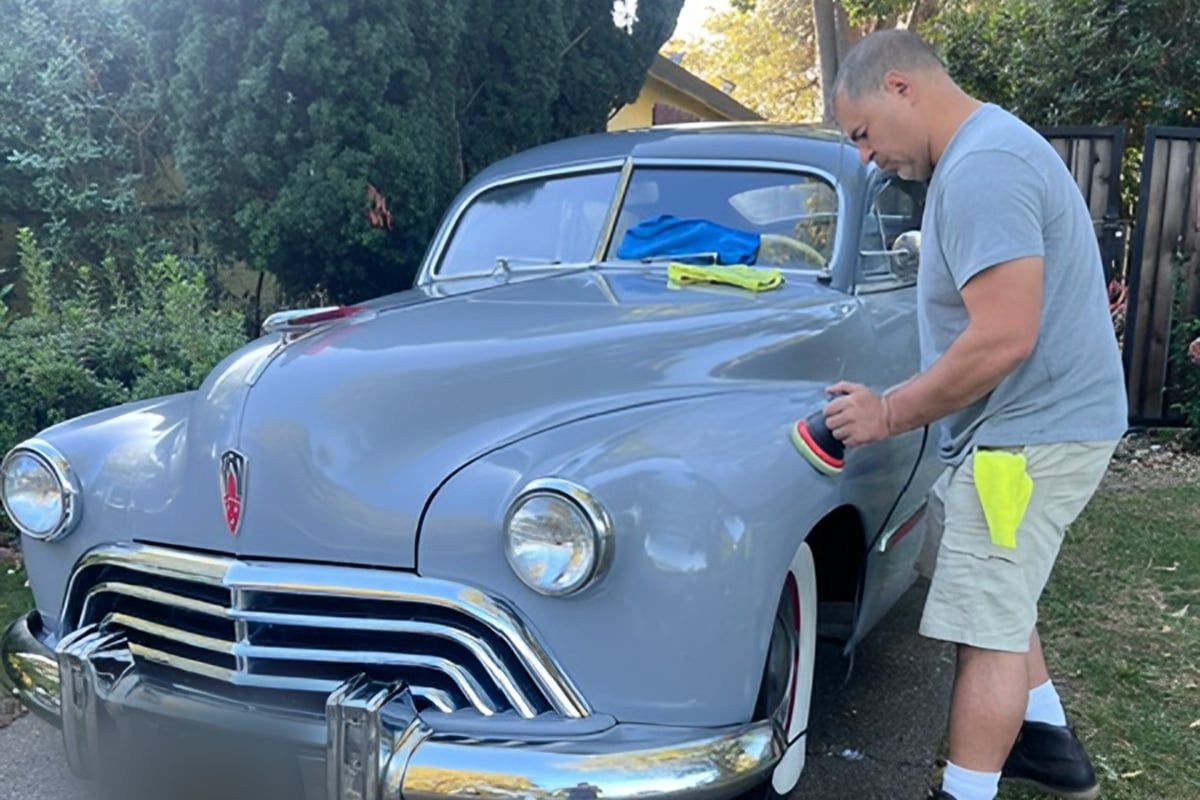 Lalo machine-polishing the front fender of a gray late-1940s Oldsmobile