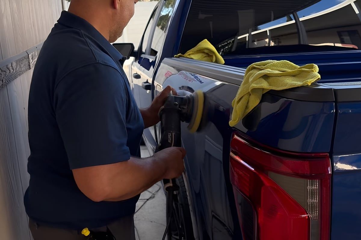 Dual-action polisher with a yellow foam pad on the bed side of a blue Ford F-150
