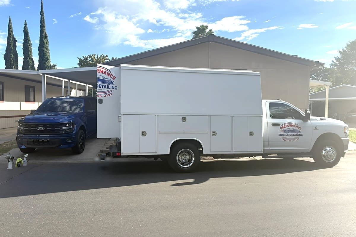 Service truck with the Performance Mobile Detailing logo parked at a curb in front of a house
