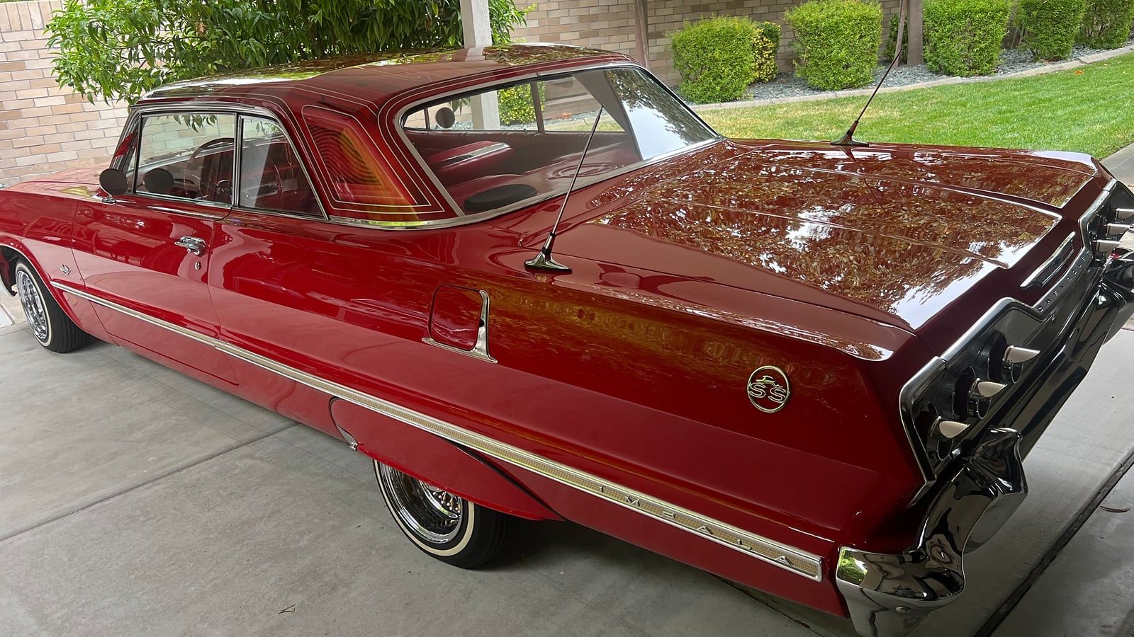 Red early-1960s Chevrolet Impala hardtop under a carport, rear three-quarter view